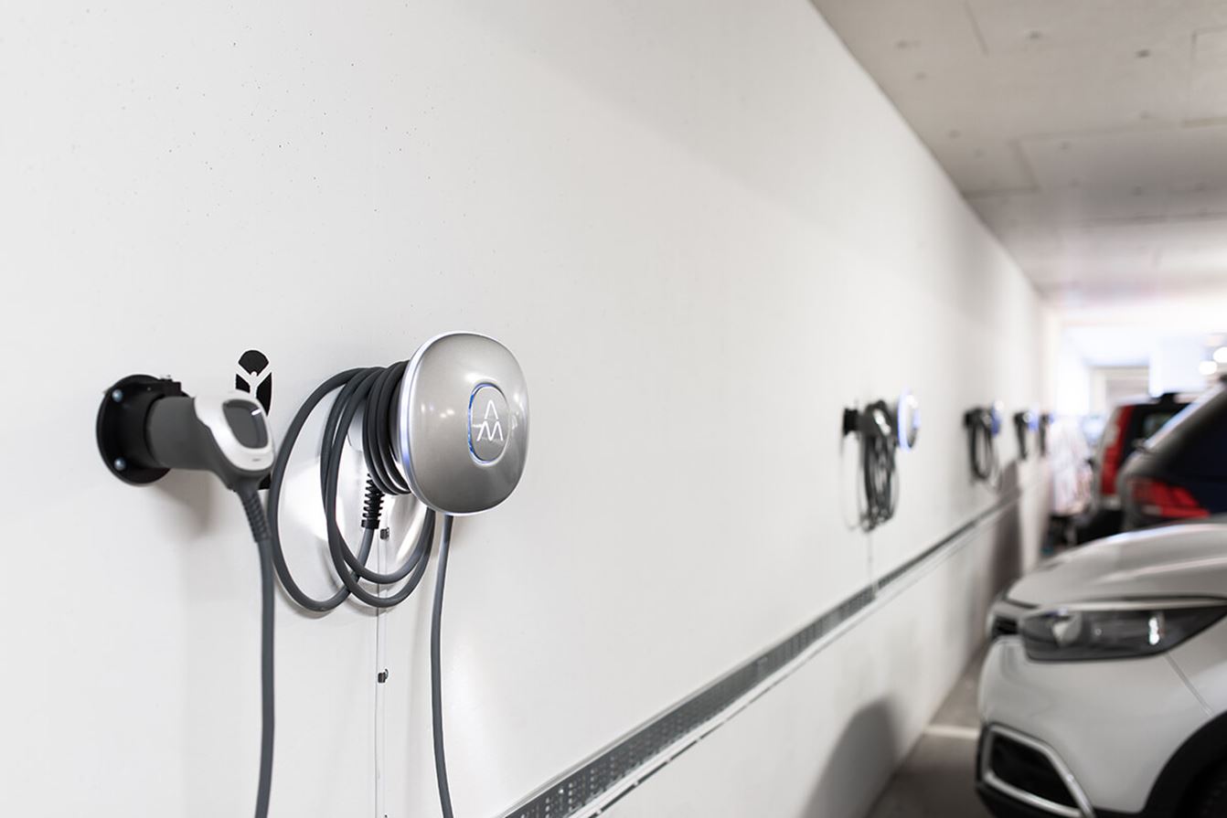 Elbilsladdare monterade på vägg i ett parkeringsgarage, med en vit elbil parkerad bredvid.