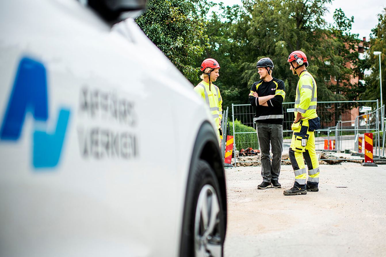 Tre personer i skyddsutrustning samtalar vid ett vägarbete. I förgrunden syns ett fordon från Affärsverken.