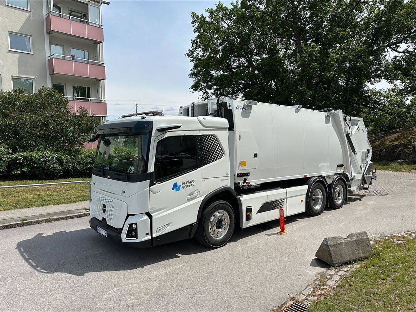 Eldriven renhållningsbil från Affärsverken står parkerad på en gata utanför ett flerbostadshus.