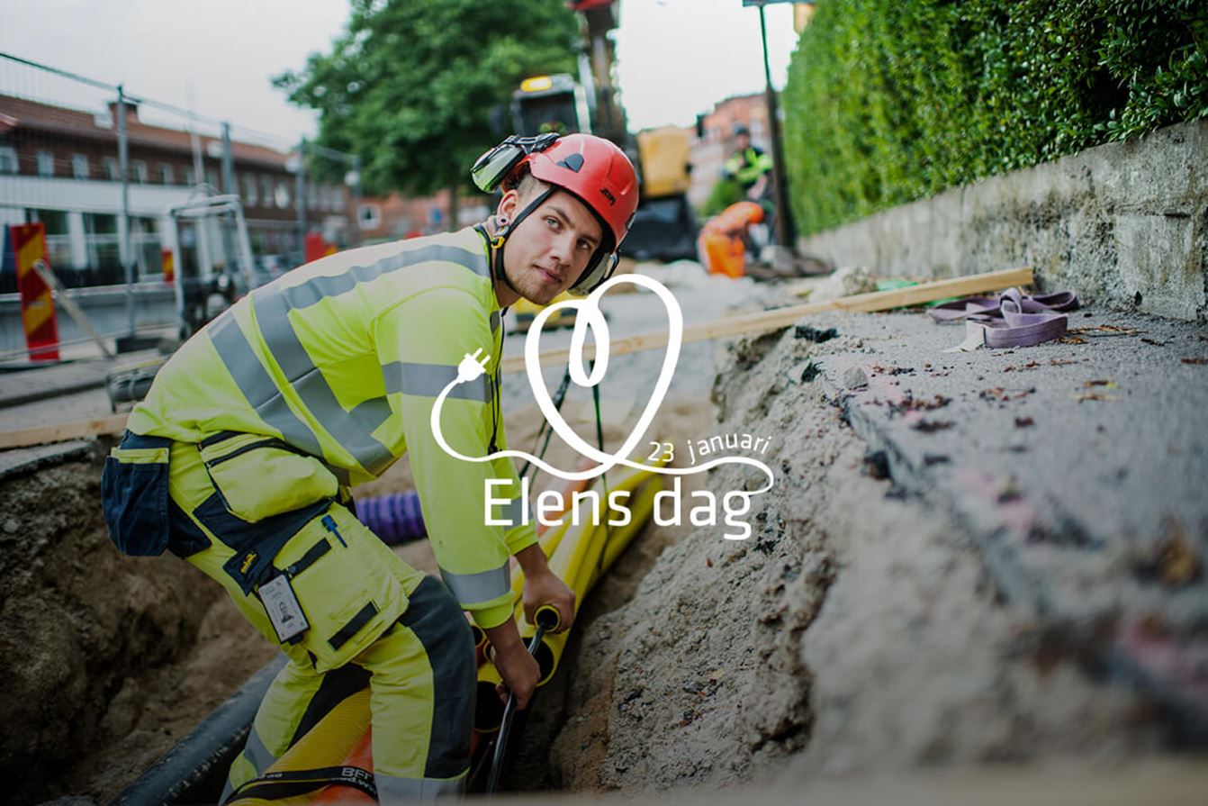 En elarbetare i varselkläder och hjälm arbetar i ett schakt vid en gata och hanterar elkablar. Bilden används för att uppmärksamma Elens dag den 23 januari 2026.